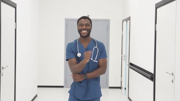 Portrait of Happy AfricanAmerican Doctor Performing a Fun Dance in the Hallway in Modern Clinic