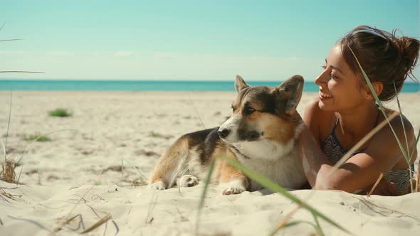 Happy Affectionate and Tender Tanned Woman in Bikini Lying on Sand at Sunny Sea Beach with Her Pet alt