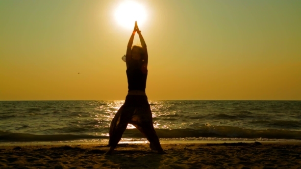 Young Woman Practicing Yoga On The Beach At Sunset