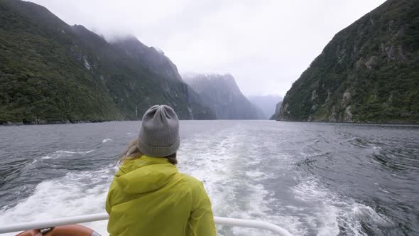 Slow motion shot of girl in yellow rain jacket on back of boat surrounded by mountains and fiords. M alt