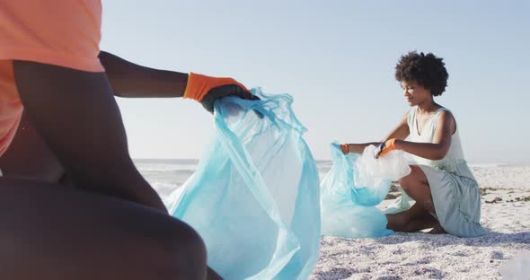 African american couple segregating waste with gloves on sunny beach alt