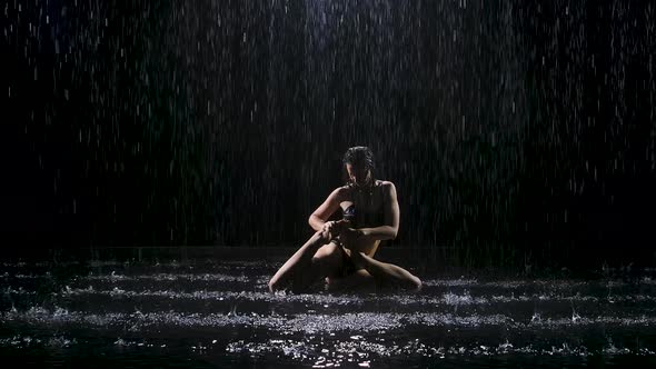 Beautiful Young Woman with Dark Hair Performs Complex Asanas Under the Streams of Rain. The Studio alt