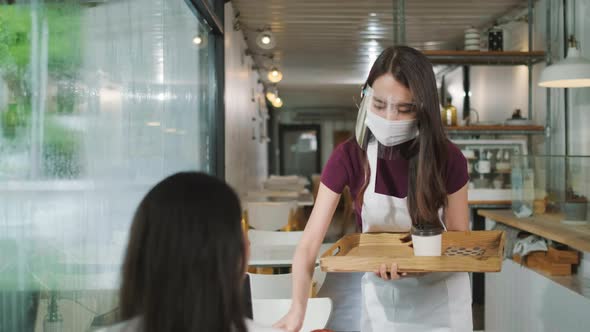 Asian waitress with face protective mask and face shield serving coffee and bread in coffee shop