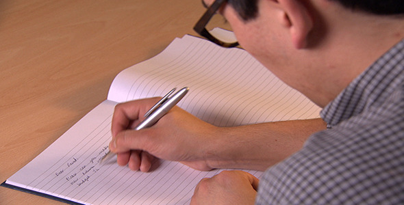 Man Writes Down Notes in Notebook