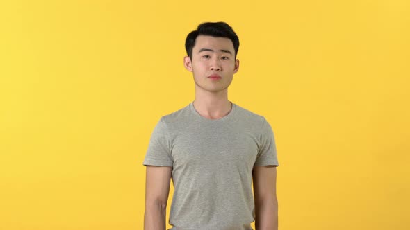 Young Asian man shrugging shoulders and rolling eyes with uncaring facial expression