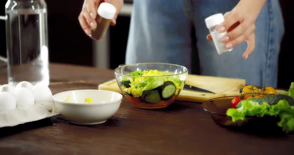 Women's Hands Pour Salt and Pepper Into a Fresh Salad in a Bowl