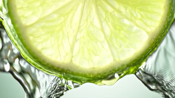 Super Slow Motion Macro Shot of Flowing Water From Lime Slice on Green Background at 1000Fps alt