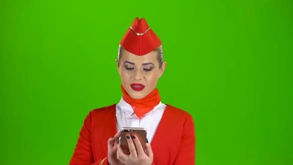 Stewardess in the Red Attire Looks Into the Phone and Is Surprised. Green Screen alt