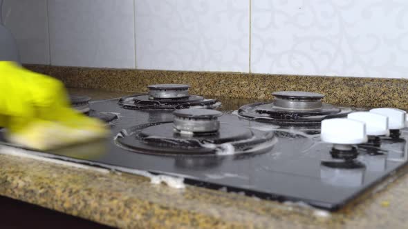 housewife woman in yellow gloves washes gas stove in kitchen with sponge. alt
