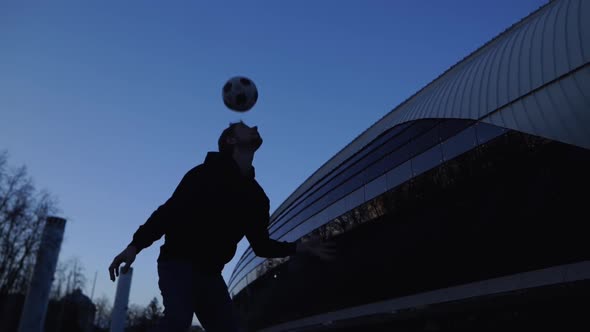 A Teenager Hits a Soccer Ball Near the Stadium with His Head