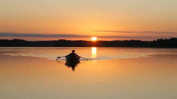 Silhouette of Fisherman Rowing on Boat at Sunset