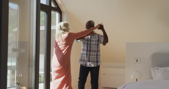 Happy senior diverse couple dancing in living room at retirement home alt