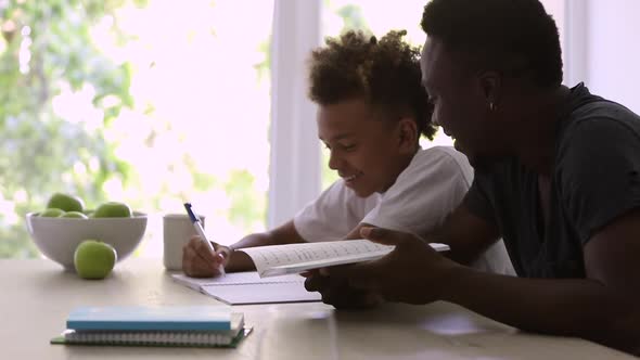 African American Man and Boy Doing Homework and Talking at Table in Apartment Interior Spbi alt