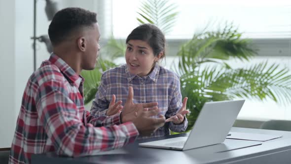 African Man and Indian Woman Arguing while Working on Laptop alt