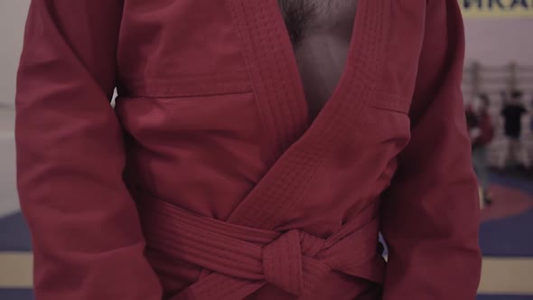 Adult Sambo Wrestler Dressed in Red Kimono Tie a Red Belt Before Fight