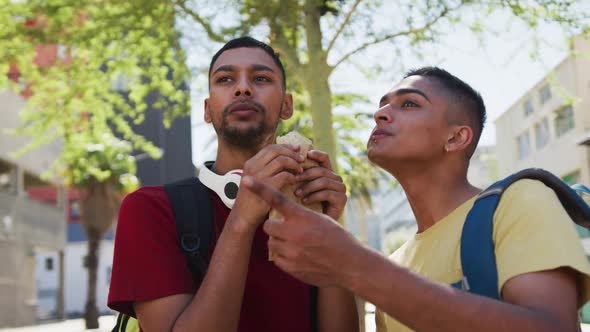 Two happy mixed race friends eating and talking in the street alt