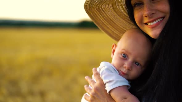 Portrait of loving mother kissing blue eyed baby in wheat field alt