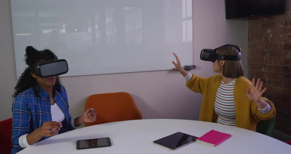 Diverse female business colleagues sitting at table using vr headsets in meeting room alt