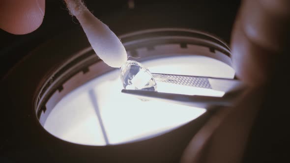 A gemologist inspecting a large clear diamond under a microscope alt