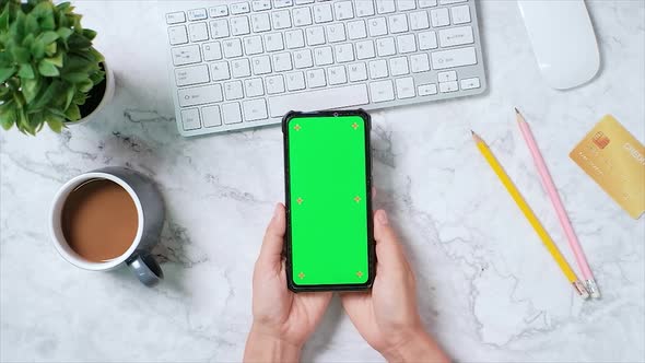 Top view, Woman hands using smartphone with mock-up chroma key green screen display on marble desk. alt