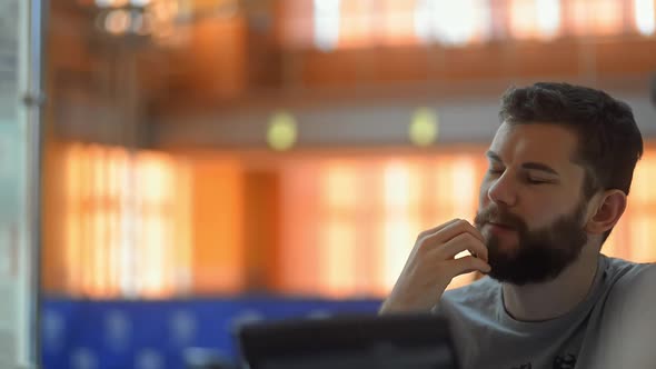 Young Bearded Man Is Talking with Colleagues, Sitting at Table in Modern Office Irrl.
