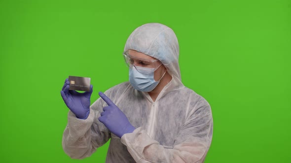 Doctor in PPE Suit with Coronavirus Vaccine Ampoule and Credit Card in Hands on Green Chroma Key alt