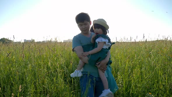 Korean Family with Their Daughter Lie in a Field in the Grass at Sunset alt