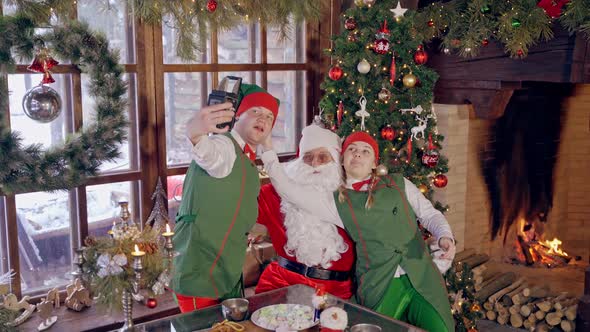 Happy elves and Santa near Christmas tree. Santa Claus together with joyful elves making photo alt