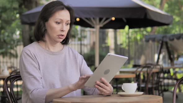 Upset Old Woman Reacting to Loss on Tablet in Outdoor Cafe alt