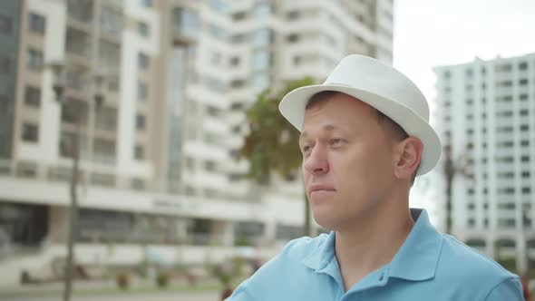 Man Stands in the Middle of City Buildings Holds a Hat with His Hand Looking at the Facades