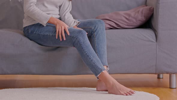 A woman is sitting on the grey couch and try to do self massage on her thigh and joint as well alt