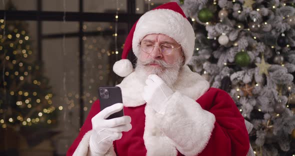 Brooding Santa Reads the Message on His Smartphone Strokes His Mustache and Looks Around Nodding His alt