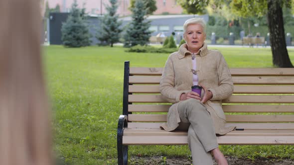 Relaxed Elderly Grandmother Drinking Coffee on Park Has Pleasant Conversation with Unrecognizable alt