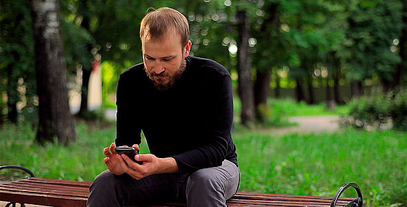 Young Man With the Phone Sitting in the Park