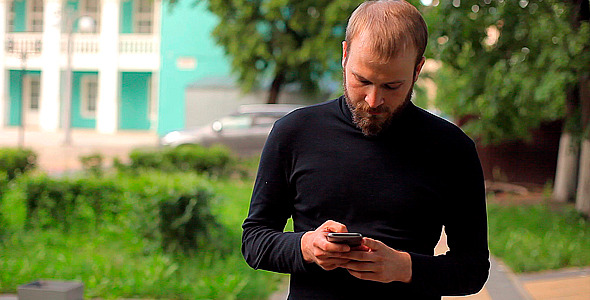 The Young Man Walking With the Phone in the Park