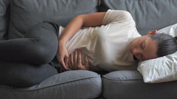 Woman with Abdomen Pain Laying on the Grey Sofa. Painful Periods. Digestive System Problems alt