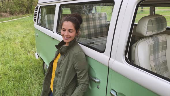 Young woman leaning on camper and smiling