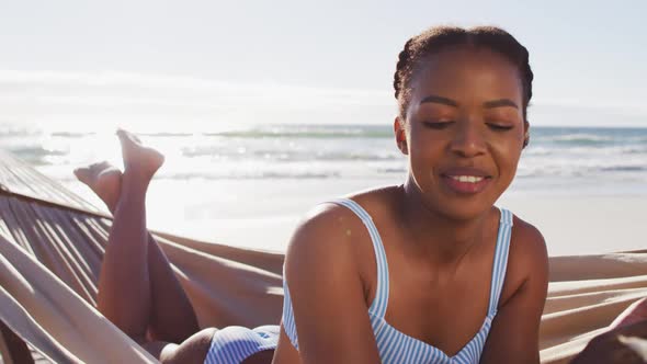 African american woman using digital tablet while lying on a hammock at the beach alt