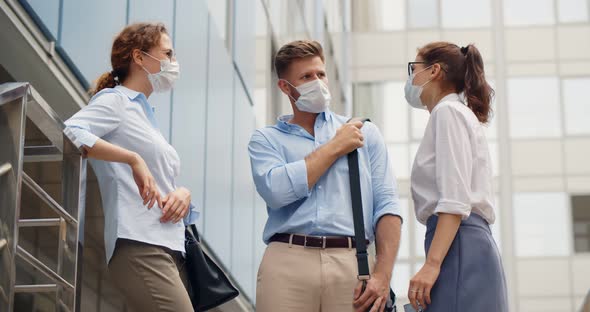 Portrait of Young Coworkers in Safety Mask Talking Outside Office Building alt