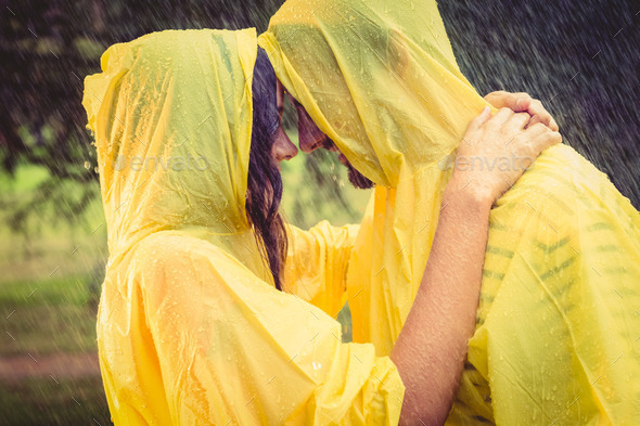 Cute couple wearing protection cape and hugging under the rain in the park - Stock Photo - Images