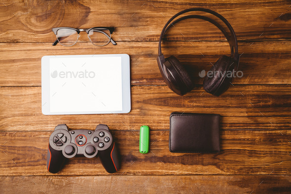Tablet and music headphone next the joystick USB key and glasses on wooden table