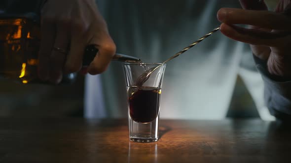 Bartender Pours Transparent Alcohol To the Layered Shot with Dakr Liquor By Bar Spoon in Slowmotion alt