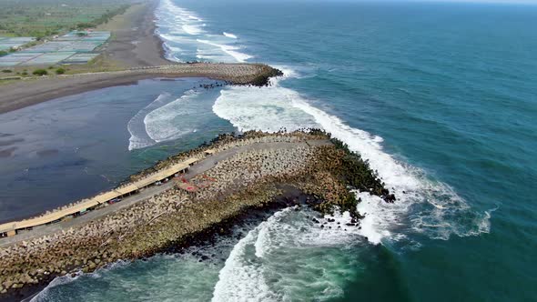 Ocean waves crashing on the breakwater pier, Glagah Beach, Indonesia, aerial alt