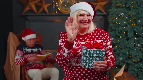 Mature Grandmother in Christmas Sweater Smiling Friendly at Camera and Waving Hands Gesturing Hello alt