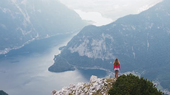 Young Woman Standing on Mountain Top and Contemplating Beautiful View of Mountain Lake alt