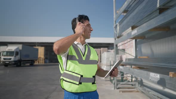 Portrait of Happy Positive Middle Eastern Expert Inspector in Headphones Walking at Warehouse alt