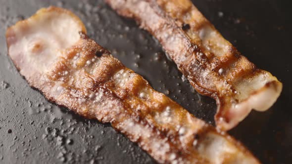 Strips of bacon, fried in oil in a pan