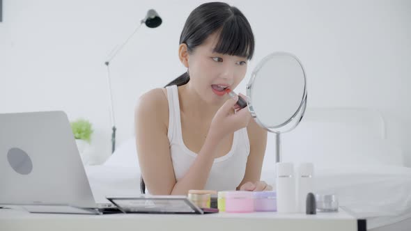 Beauty of asian woman with learning makeup with lipstick on mouth watching laptop with tutorial. alt