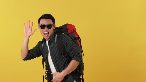 Asian man with backpack and sunglasses taking photos and waving hand