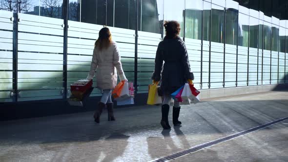 Two Girlfriends with Bags in Their Hands are Walking Down Street